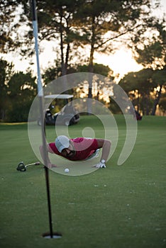 Golf player blowing ball in hole with sunset in background