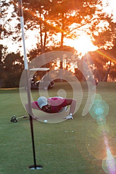 Golf player blowing ball in hole with sunset in background