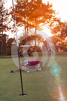 Golf player blowing ball in hole with sunset in background