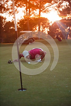 Golf player blowing ball in hole with sunset in background