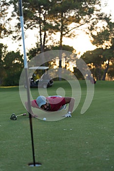 Golf player blowing ball in hole with sunset in background