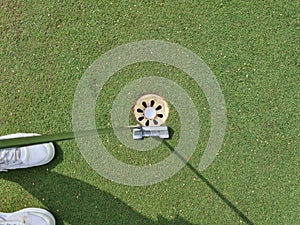 Golf player with putter and ball in hole on green