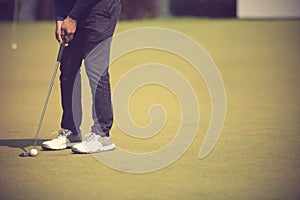 Golf player at the putting green hitting ball into a hole.