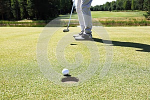 Golf player at the putting green hitting ball into a hole