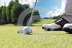 Golf player at the putting green hitting ball into a hole