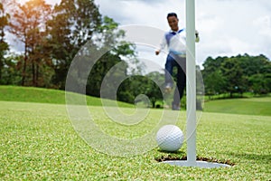 Golf player at the putting green hitting ball into a hole