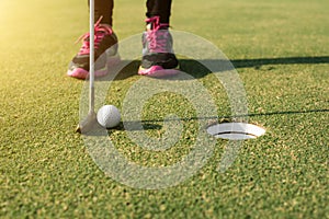 Golf player at the putting green putting golf ball into a hole.