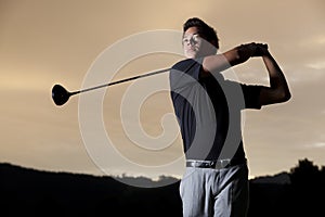 Golf player teeing off at sunset.
