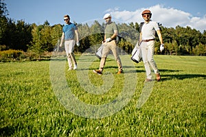 Golf player walking and carrying bag on course during summer gam