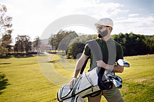 Golf player walking and carrying bag on course during summer gam