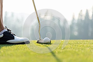 Golf player women at the putting green hitting ball into a hole in holiday sunny day.