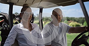 Golf players looking camera at cart. Couple sitting buggy on club course field.