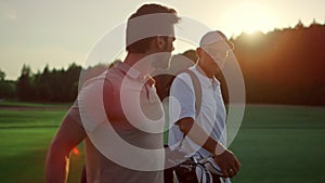 Golf players looking sunset on summer field. Golfers group walk course fairway.