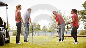 Golf Professional Demonstrating Shot On Fairway To Group Of Golfers During Lesson