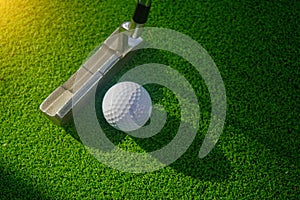 Golf ball and putter on green grass background in the morning, with the beautiful sunlight