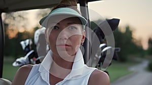 Golf woman looking camera at nature. Beautiful golfer sit in buggy car on course