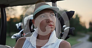 Golf woman looking camera at nature. Beautiful golfer sit in buggy car on course