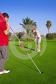 Golf woman putting gol ball and man holds flag