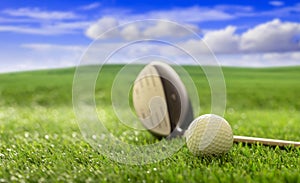 Golfball and stick on green grass golf course, blue cloudy sky background