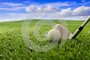 Golfball and stick on green grass golf course, blue cloudy sky background