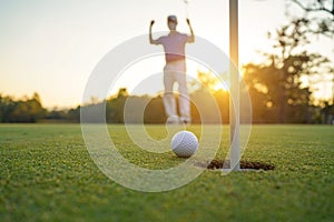 Golfer action to win after long putting golf ball on the green golf, lens flare on sun set evening time