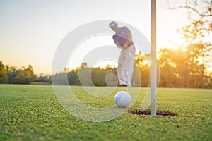 Golfer action to win after long putting golf ball on the green golf, lens flare on sun set evening time