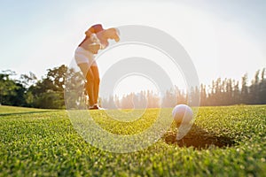 Golfer asian woman focus putting golf ball on the green golf on sun set evening time photo