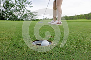 Golfer asian woman sporty putting golf ball into hole on the green golf