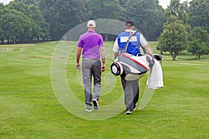 Golfer and caddy walking up a fairway