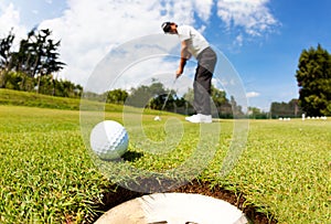 Golfer drove the ball into the hole on putting green; summer sun