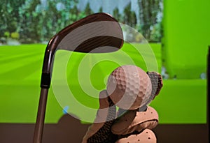 Golfer in glove holds golf ball and club indoors