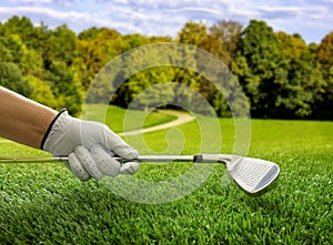 Golfer hand in glove holding a club, close up view. Golf course, blue sky background