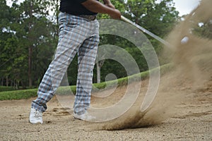 Golfer hitting golf ball on bunker of sand in course