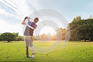 Golfer hitting golf shot with club on course at evening time.