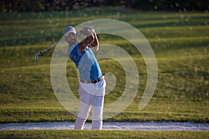 Golfer hitting a sand bunker shot on sunset