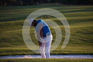 Golfer hitting a sand bunker shot on sunset