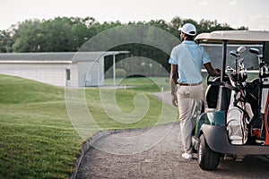 Golfer looking away while standing near golf cart