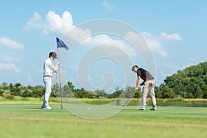 Golfer man and friend playing golf aiming shot for putting ball on the hole with club on green course.