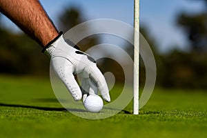 Golfer man hand with golf glove. Golf ball near hole. Golf ball on lip of cup on grass background.