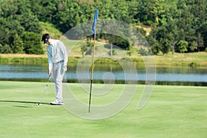 Golfer man playing golf aiming shot for putting ball on the hole with club on green course.
