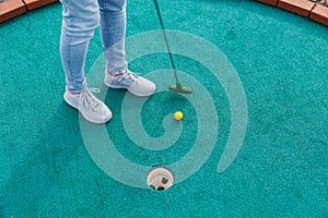 Golfer playing adventure or mini golf and trying putting ball into hole