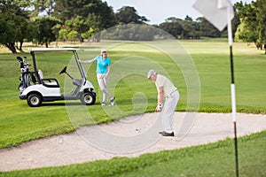 Golfer playing on sand trap by woman