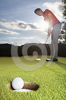 Golfer putting ball into cup.