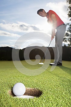 Golfer putting ball into cup.