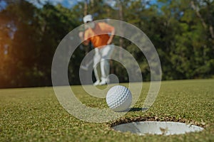 Golfer putting ball on the green golf, lens flare on sun set evening time. Golfer action to win after long putting golf ball in to