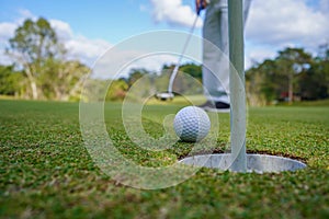 Golfer putting ball on the green golf, lens flare on sun set evening time. Golfer action to win after long putting golf ball in to