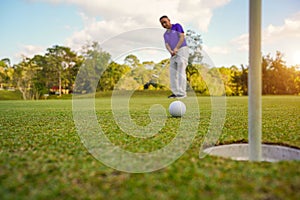 Golfer putting ball on the green golf, lens flare on sun set evening time. Golfer action to win after long putting golf ball in to