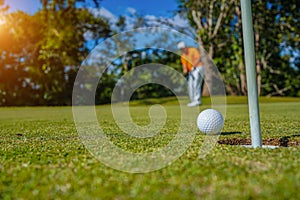 Golfer putting ball on the green golf, lens flare on sun set evening time. Golfer action to win after long putting golf ball in to