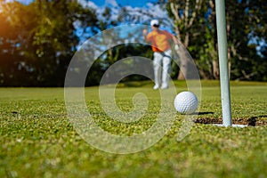 Golfer putting ball on the green golf, lens flare on sun set evening time. Golfer action to win after long putting golf ball in to