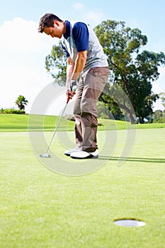 Golfer about to putt the ball. Full length of man playing golf and taking position to putt the ball in the hole.